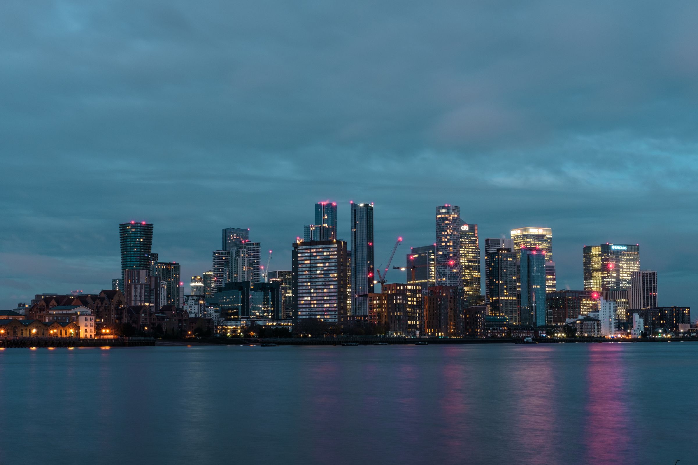 Canary Wharf at night across the Thames, with warm lights against a blue sky